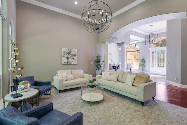 living room featuring hardwood / wood-style floors, crown molding, ornate columns, and a notable chandelier