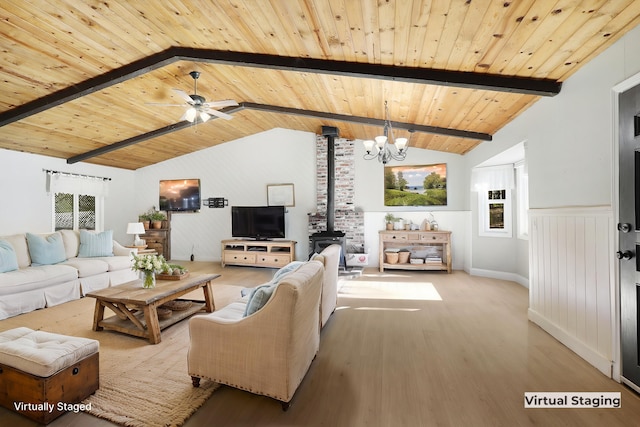 living room with ceiling fan with notable chandelier, lofted ceiling with beams, a wood stove, wood ceiling, and light hardwood / wood-style floors