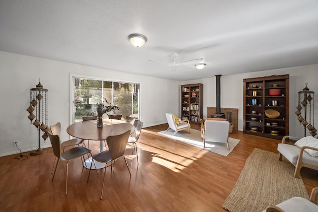 dining area with ceiling fan, a wood stove, and light hardwood / wood-style floors