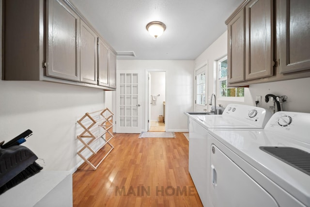 clothes washing area with cabinets, sink, washing machine and dryer, and light wood-type flooring