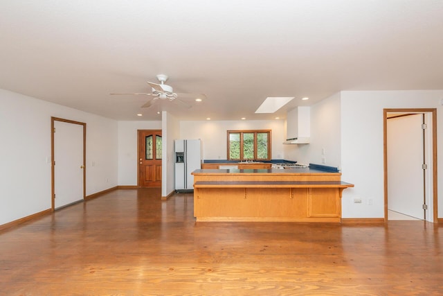 kitchen featuring a skylight, a kitchen bar, kitchen peninsula, white refrigerator with ice dispenser, and white cabinets