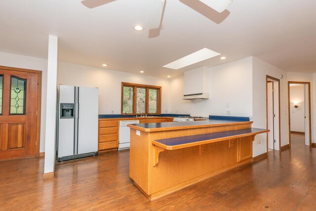 kitchen with a skylight, kitchen peninsula, white appliances, wood-type flooring, and white cabinets