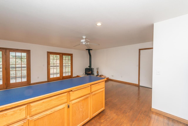 kitchen with ceiling fan, light brown cabinetry, dark wood-type flooring, and a wood stove