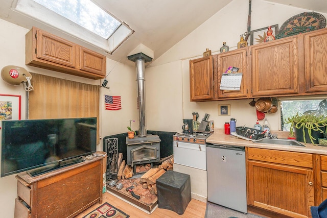 kitchen with vaulted ceiling with skylight, dishwasher, a wood stove, sink, and stainless steel refrigerator