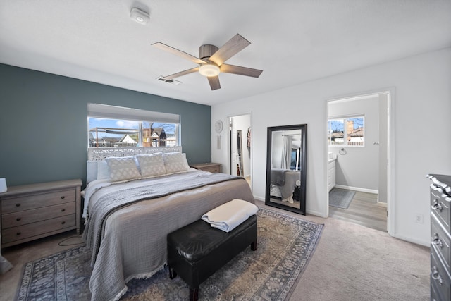 carpeted bedroom featuring multiple windows, ensuite bath, and ceiling fan