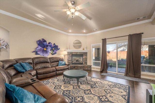 living room featuring crown molding, ceiling fan, dark hardwood / wood-style floors, and a stone fireplace