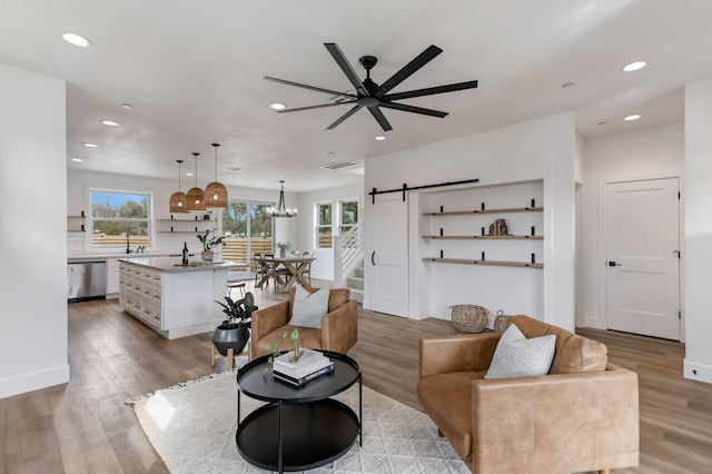 living room with a barn door, sink, ceiling fan with notable chandelier, and light hardwood / wood-style flooring