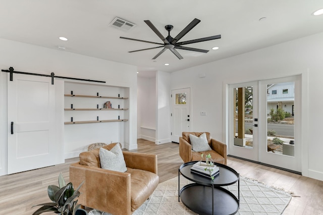 living room featuring ceiling fan, a barn door, and light hardwood / wood-style floors