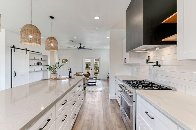 kitchen featuring white cabinetry, decorative light fixtures, a barn door, light stone countertops, and high end stove