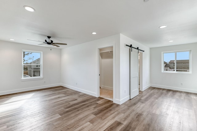 empty room featuring a barn door, ceiling fan, and light hardwood / wood-style flooring