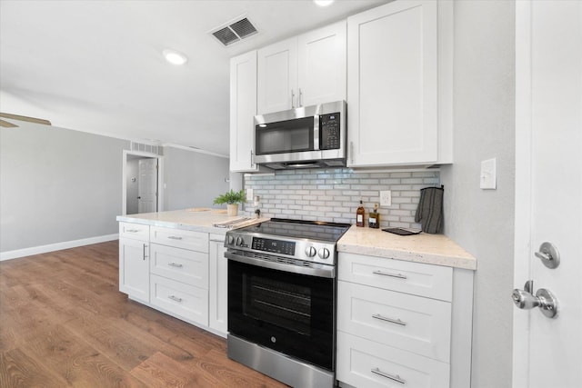 kitchen featuring tasteful backsplash, light stone counters, hardwood / wood-style flooring, stainless steel appliances, and white cabinets