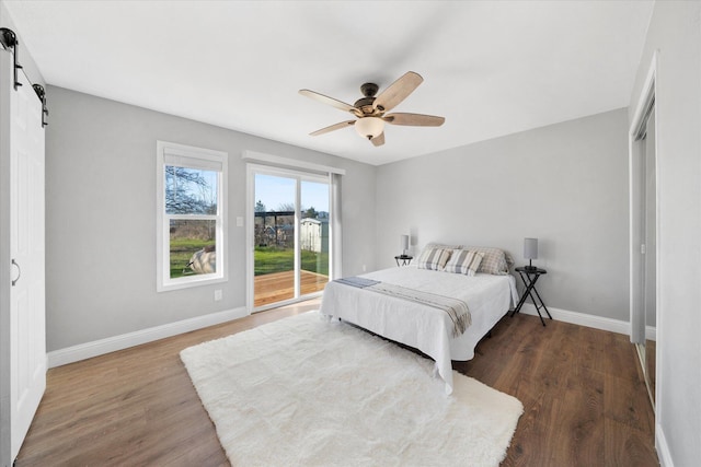 bedroom featuring dark wood-type flooring, ceiling fan, a barn door, and access to outside