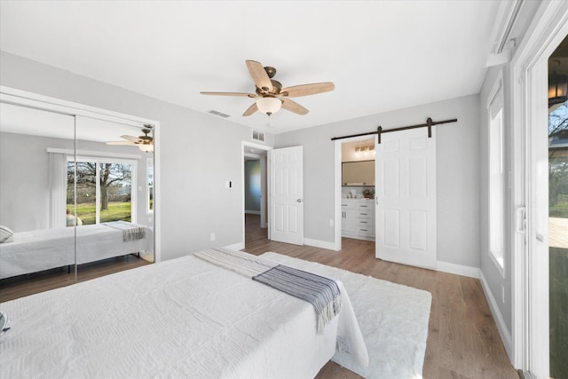 bedroom with a closet, wood-type flooring, a barn door, and ceiling fan