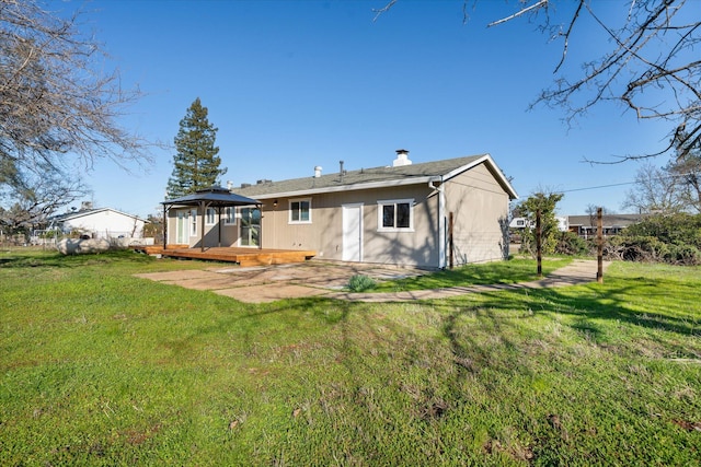 back of property with a gazebo, a wooden deck, a patio, and a lawn