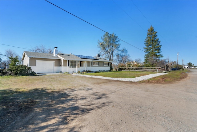 ranch-style home with a garage, a front yard, and solar panels