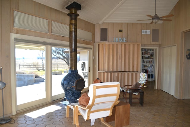 living area with ceiling fan, wooden walls, and vaulted ceiling