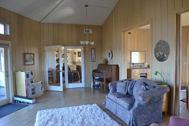 living room featuring light hardwood / wood-style floors, wood walls, a notable chandelier, french doors, and high vaulted ceiling