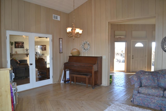 entryway featuring wood walls, light parquet floors, french doors, and a notable chandelier