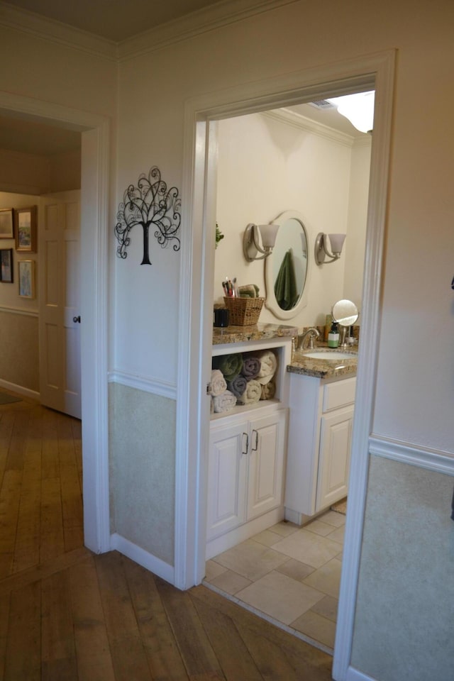 corridor featuring light wood-type flooring, sink, and crown molding