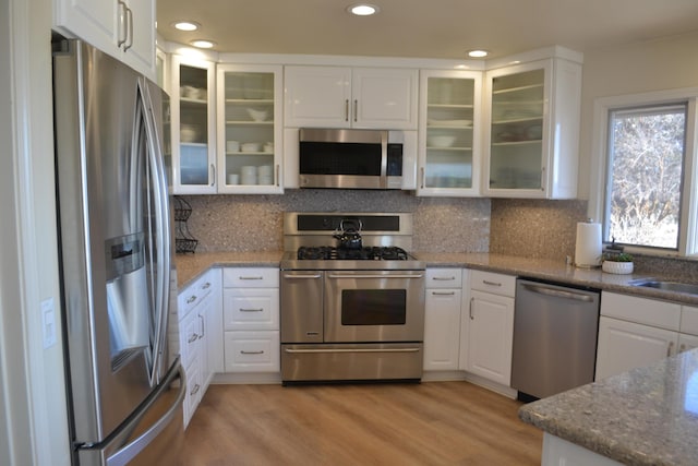 kitchen with light stone countertops, light wood-type flooring, appliances with stainless steel finishes, and white cabinetry