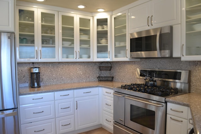 kitchen with stainless steel appliances, backsplash, white cabinetry, and light stone counters