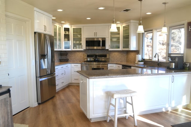 kitchen featuring decorative light fixtures, white cabinetry, stainless steel appliances, dark stone countertops, and kitchen peninsula