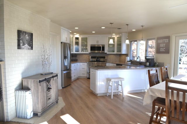 kitchen with decorative light fixtures, a kitchen bar, kitchen peninsula, white cabinetry, and stainless steel appliances