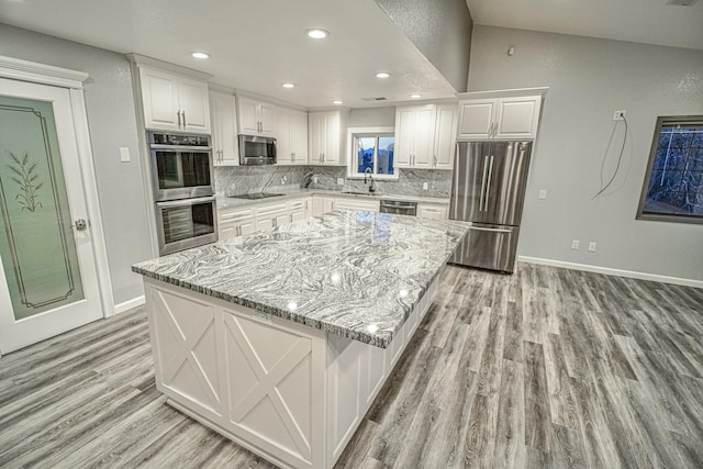 kitchen with appliances with stainless steel finishes, white cabinets, a kitchen island, and light stone countertops