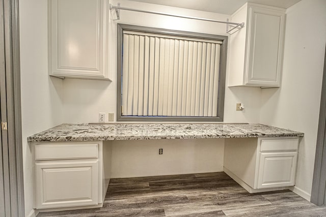 interior space featuring dark wood-type flooring, white cabinetry, built in desk, and light stone counters