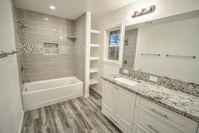 bathroom with wood-type flooring, vanity, and tiled shower / bath