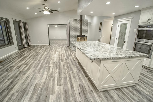 kitchen with white cabinets, vaulted ceiling, a spacious island, and stainless steel double oven