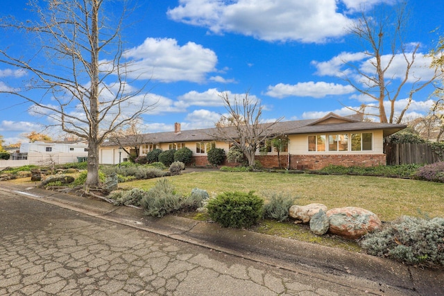 view of front of home with brick siding, a chimney, fence, a garage, and a front lawn