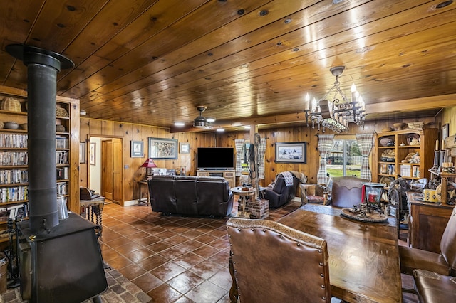 dining space with wood ceiling, a wood stove, built in shelves, ceiling fan with notable chandelier, and wood walls