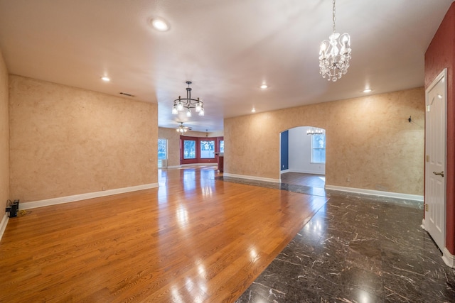 unfurnished room with ceiling fan with notable chandelier and wood-type flooring