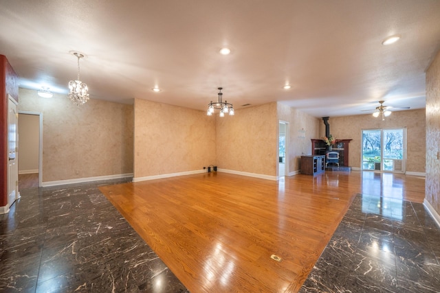 unfurnished living room with ceiling fan with notable chandelier and a wood stove