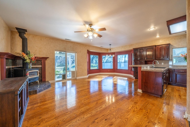 kitchen featuring pendant lighting, sink, a wood stove, ceiling fan, and light hardwood / wood-style flooring