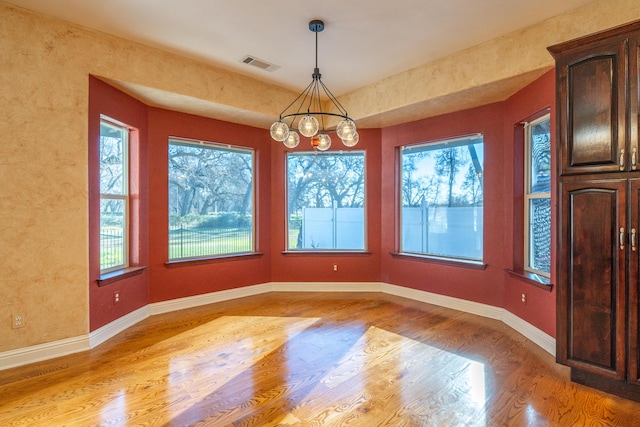 unfurnished dining area featuring plenty of natural light, a notable chandelier, and light wood-type flooring