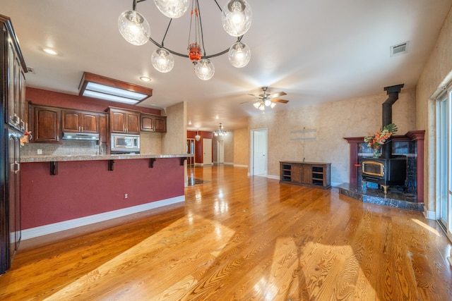 kitchen with pendant lighting, a breakfast bar area, stainless steel microwave, light stone countertops, and light wood-type flooring