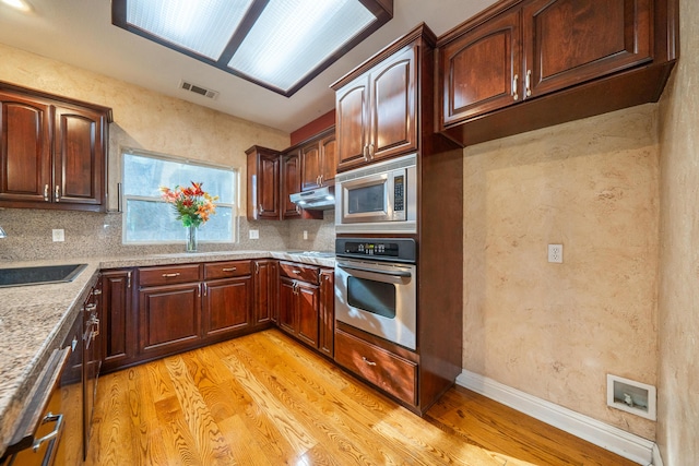 kitchen with sink, stainless steel appliances, light stone counters, decorative backsplash, and light wood-type flooring