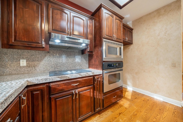 kitchen with stainless steel appliances, tasteful backsplash, light stone countertops, and light wood-type flooring