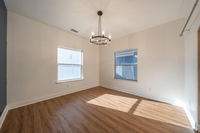 empty room with wood-type flooring and a notable chandelier