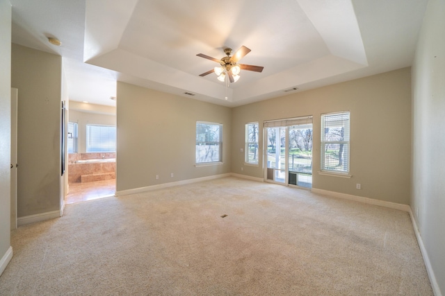 carpeted empty room with ceiling fan, a healthy amount of sunlight, and a raised ceiling