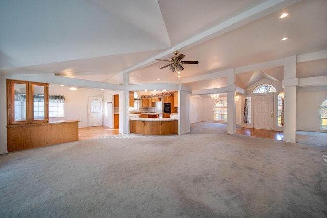 unfurnished living room featuring ceiling fan with notable chandelier, light colored carpet, decorative columns, and vaulted ceiling with beams