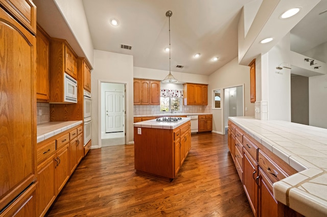 kitchen featuring decorative light fixtures, tasteful backsplash, white appliances, a center island, and tile counters