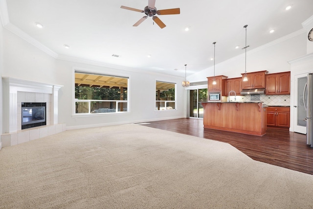 carpeted living room with sink, crown molding, vaulted ceiling, ceiling fan, and a fireplace