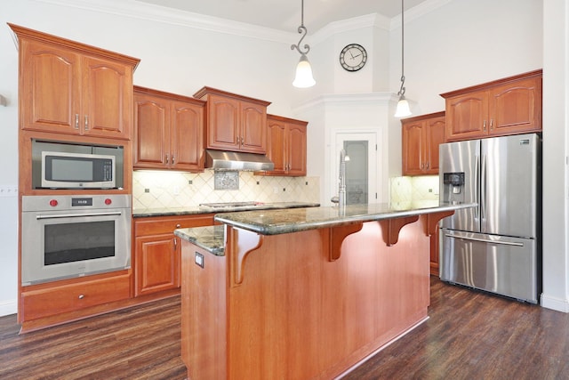 kitchen featuring tasteful backsplash, decorative light fixtures, a center island with sink, a kitchen breakfast bar, and stainless steel appliances