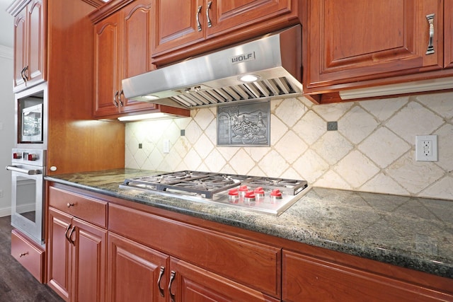 kitchen with dark wood-type flooring, appliances with stainless steel finishes, decorative backsplash, and dark stone countertops