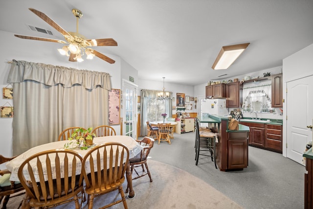 carpeted dining area with sink and ceiling fan with notable chandelier