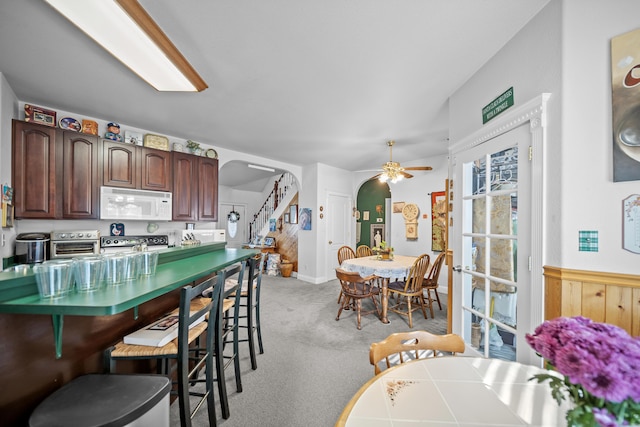 kitchen with a breakfast bar area, stove, light colored carpet, ceiling fan, and dark brown cabinets