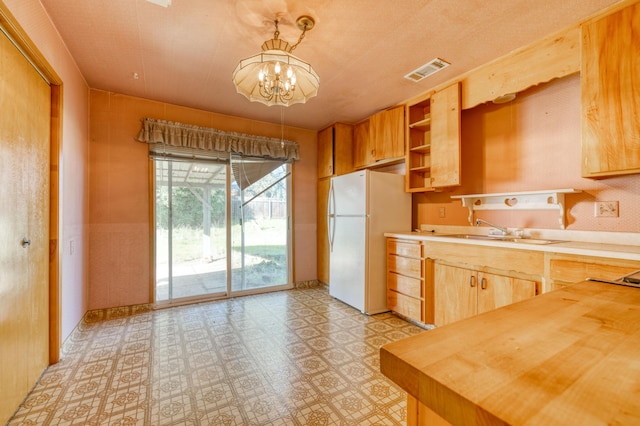 kitchen with refrigerator, butcher block countertops, decorative light fixtures, sink, and a chandelier